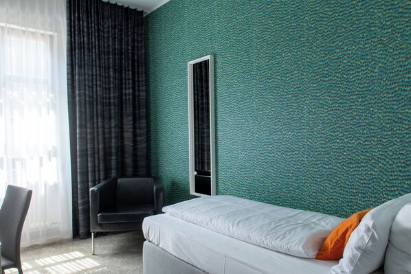 A hotel room with a bed, a chair, a window with curtains, and a textured green wall. - Hotel Maxplatz (Hof)