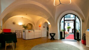 A hotel lobby with arched ceilings, a reception desk, a red carpet, and a view of the outside. - Hotel Maxplatz (Hof)
