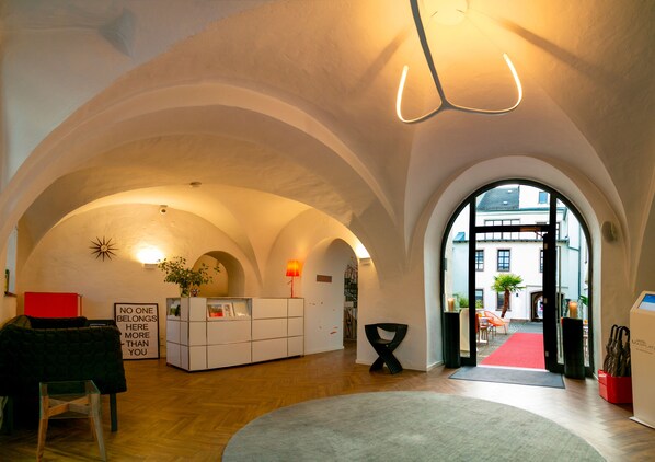 A hotel lobby with arched ceilings, a reception desk, a red carpet, and a view of the outside. - Hotel Maxplatz (Hof)