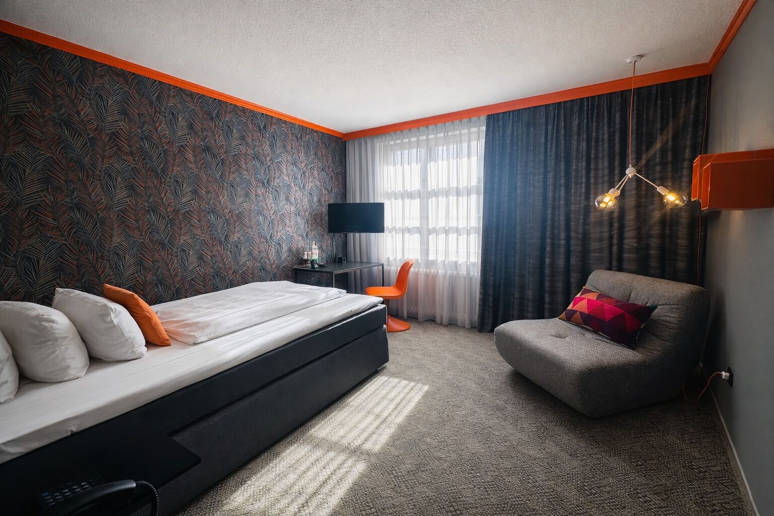 Una habitación de hotel moderna con una cama grande, una zona de estar, un televisor y una ventana con cortinas.