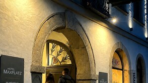 A hotel entrance with an arched doorway, a sign reading 'Hotel Maxplatz,' and a 'HAAR-KUNST' sign in the background. - Hotel Maxplatz (Hof)