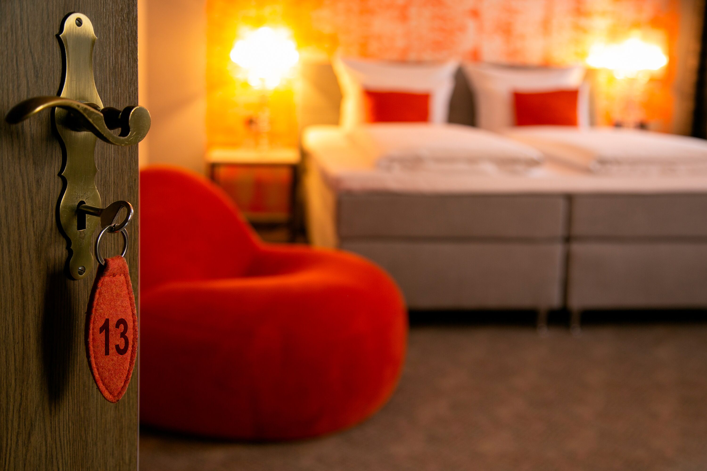 Een hotelkamer met een bed, een rode relaxstoel en een sleutelhanger met het getal 13.