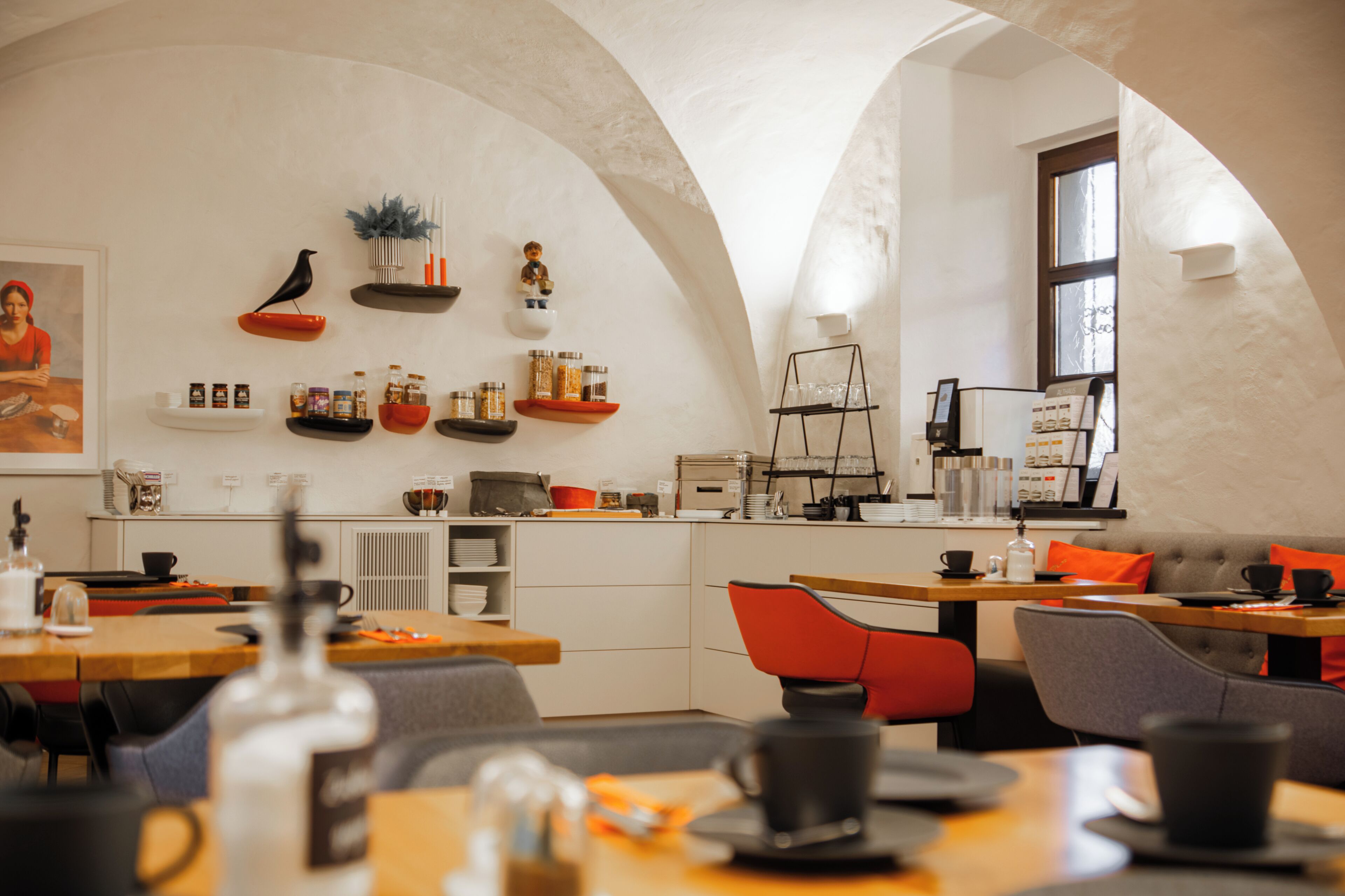 A modern interior with arched ceilings, a dining area with tables and chairs, and a kitchen area with shelves and jars.