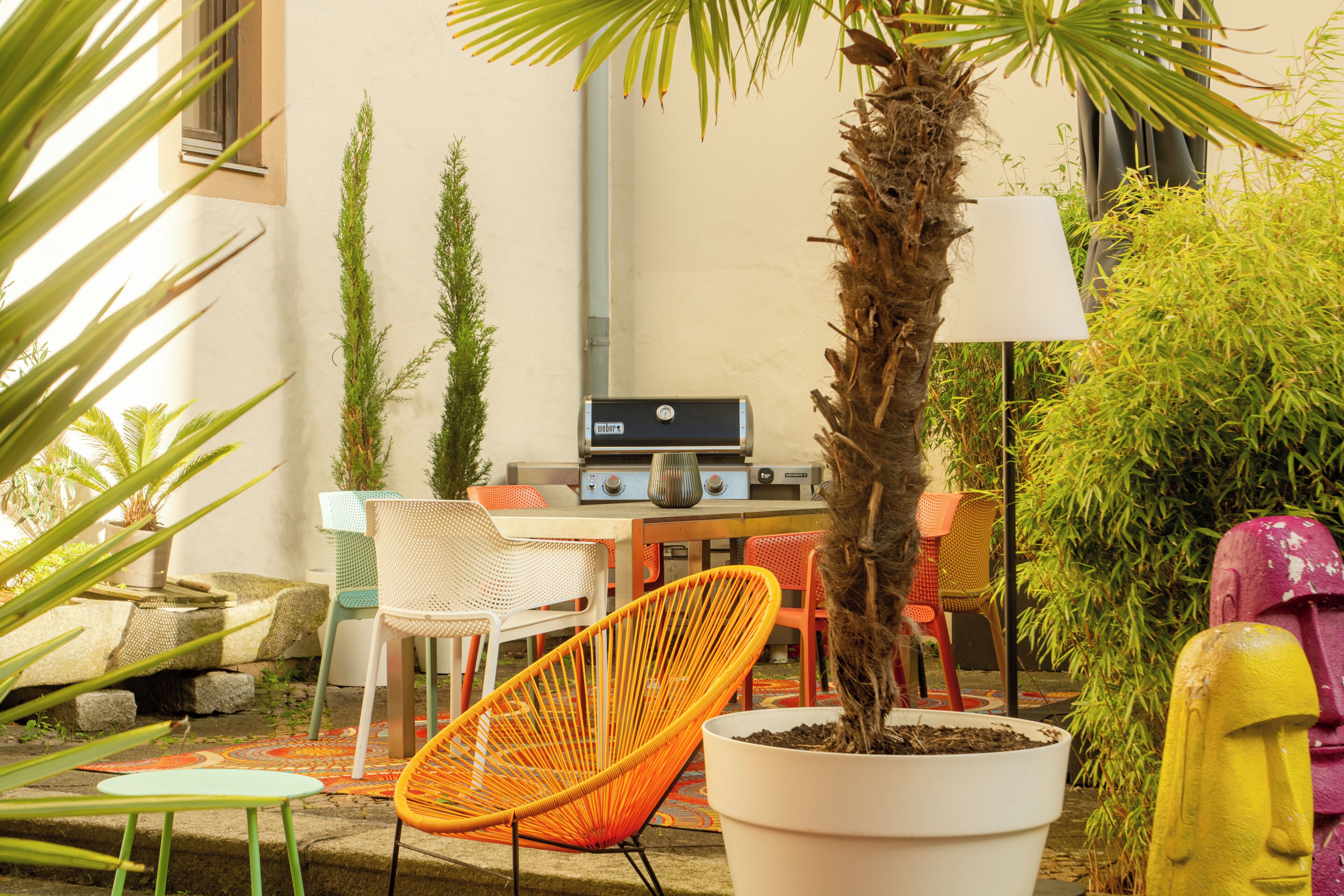 An outdoor patio with a grill, chairs, and potted plants.