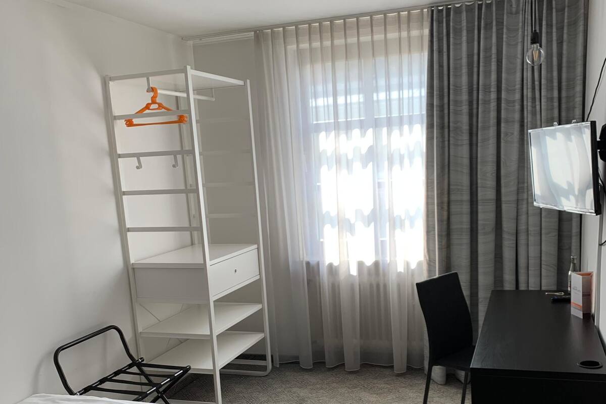 A hotel room with a bed, a desk, a chair, a wardrobe, and a TV.