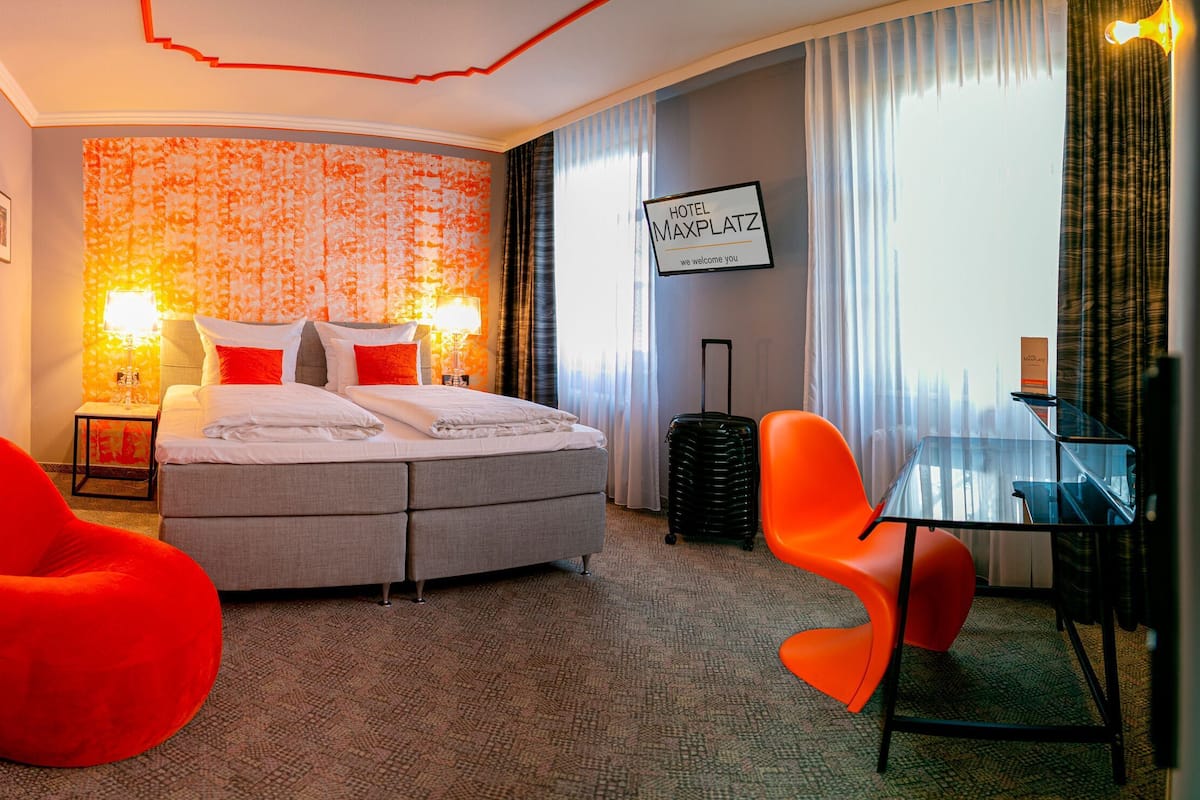A hotel room with a bed, two chairs, a desk, and a wall with a sign.