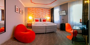 A hotel room with a bed, a red bean bag chair, a glass table, and a suitcase. - Hotel Maxplatz (Hof)