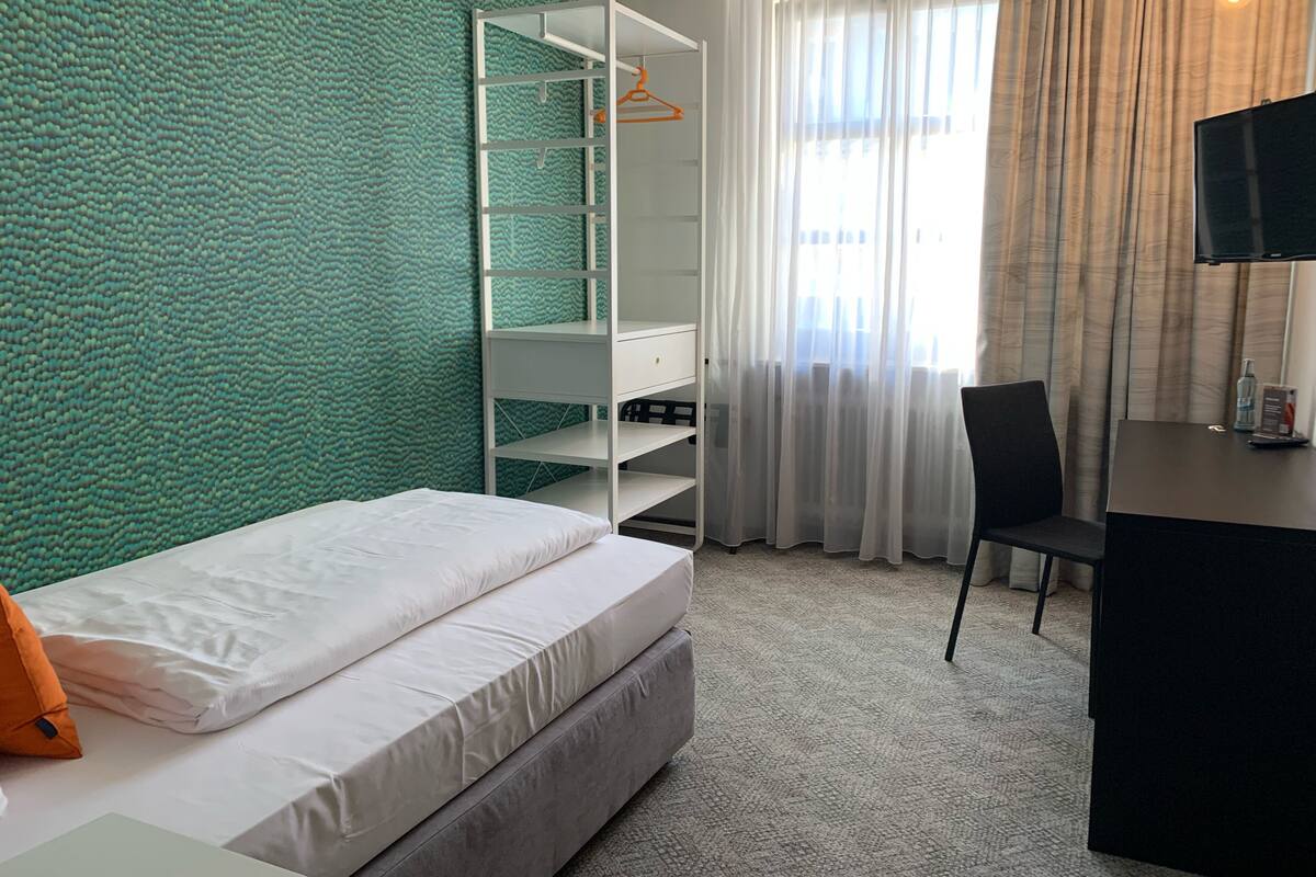 A hotel room with a bed, a desk, a chair, a wardrobe, and a TV.