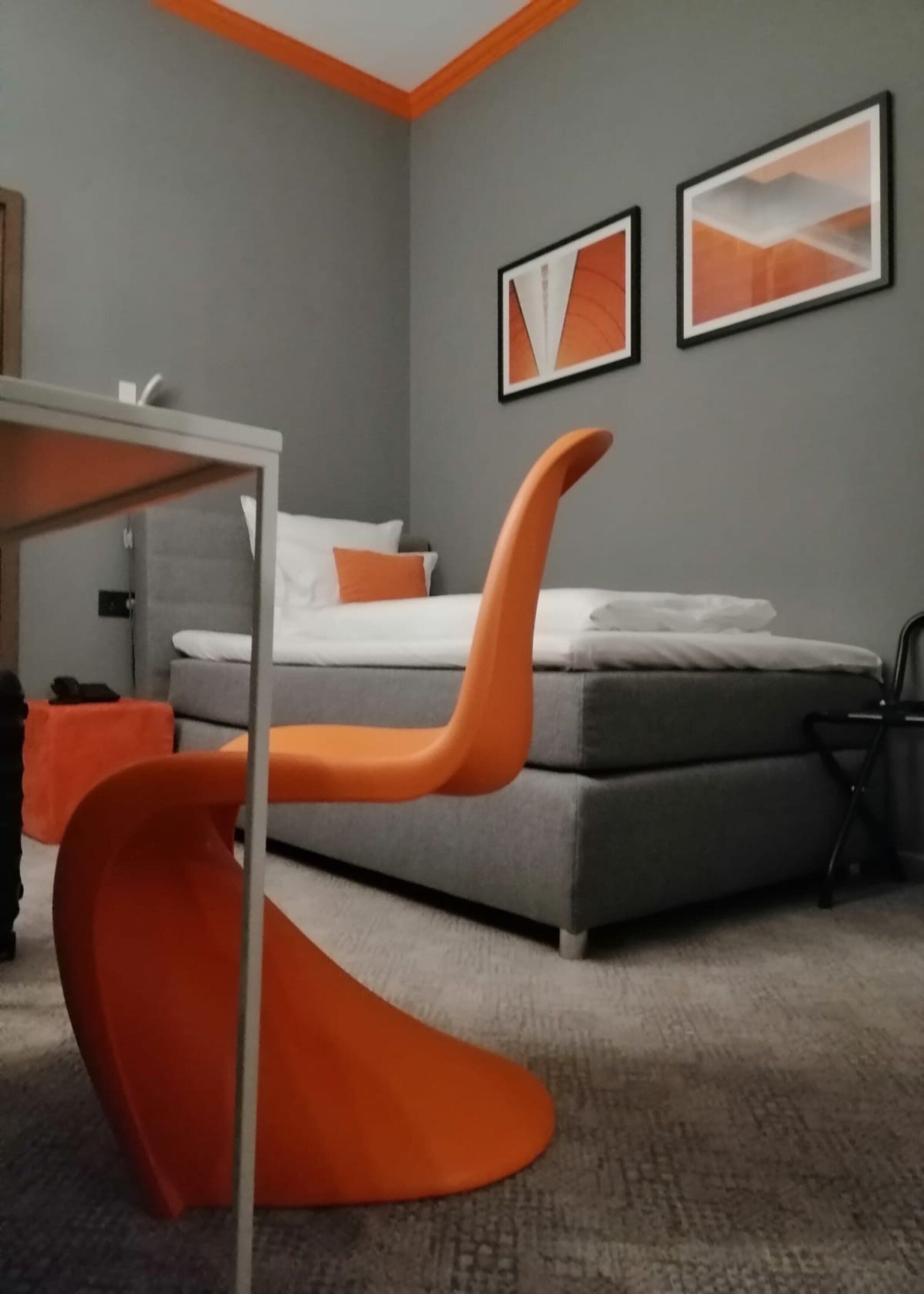 A modern bedroom with a grey sofa bed, orange furniture, and abstract wall art.