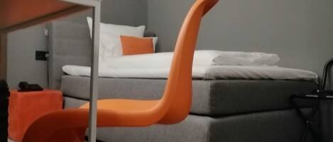 A modern bedroom with a grey sofa bed, orange furniture, and abstract wall art.