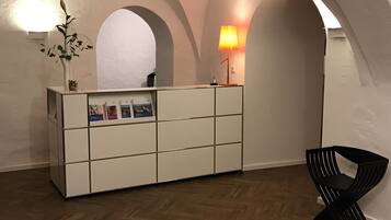 Un mostrador de recepción con una planta, una lámpara y una silla en una habitación con techos abovedados y suelo de madera.