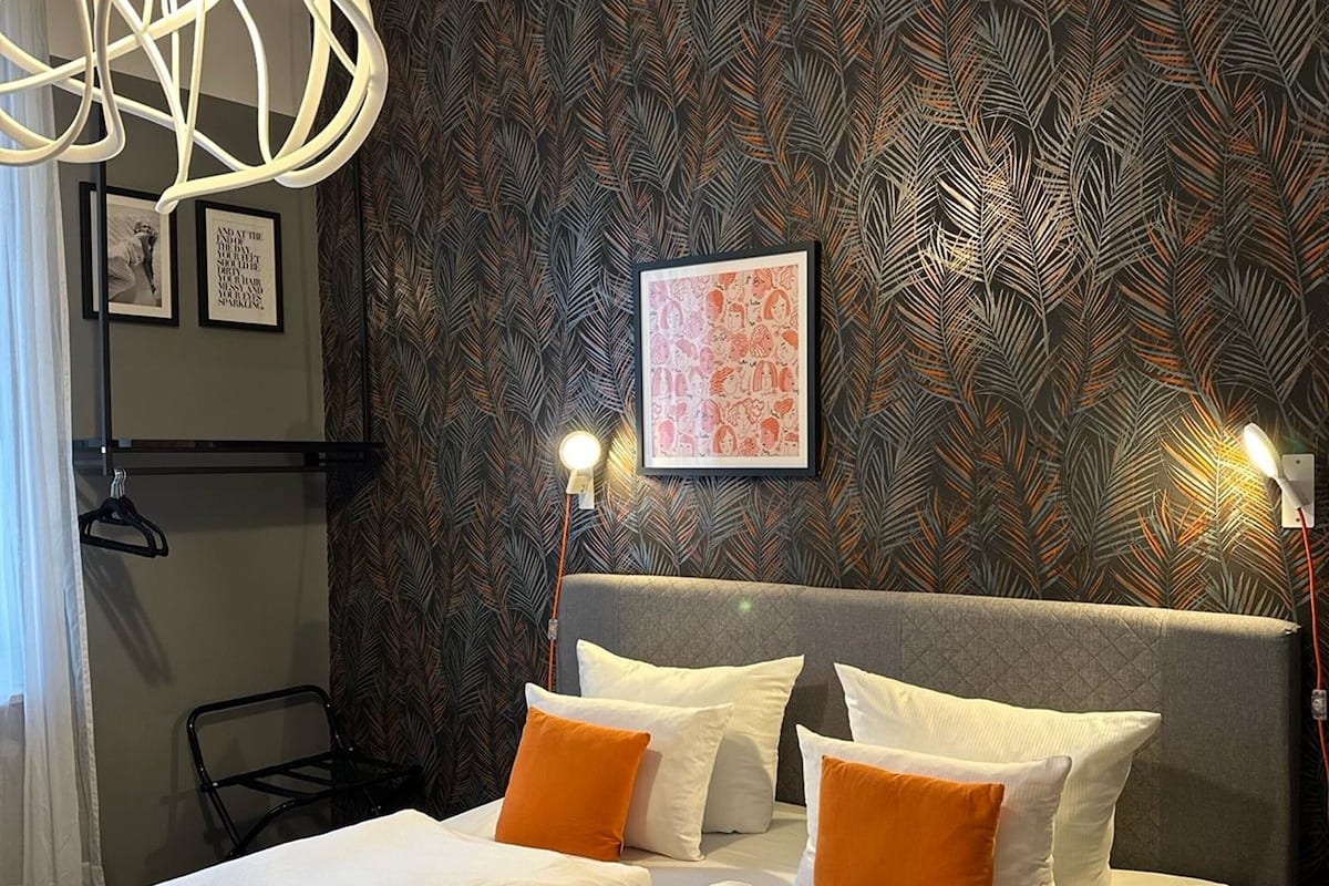 A modern hotel room with a large bed, two bedside tables, a unique ceiling light fixture, and a patterned wallpaper.
