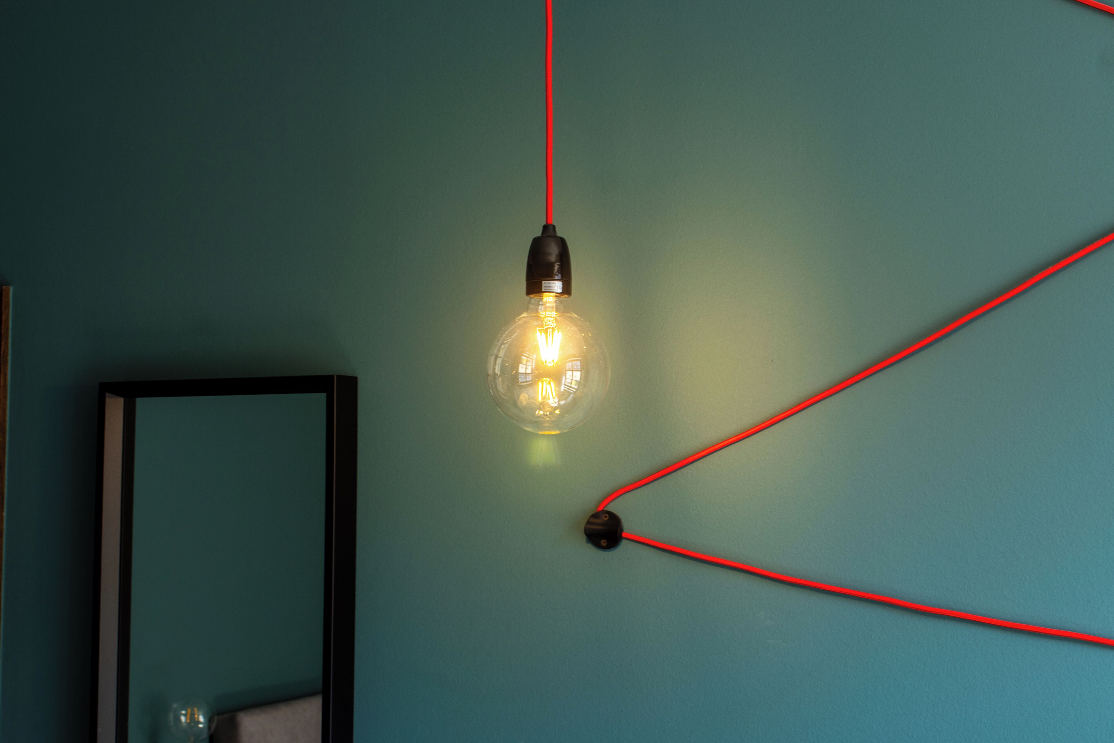 Una bombilla con un cable rojo frente a una pared verde azulado.