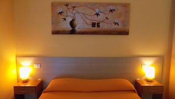 A hotel room with a bed, two bedside tables with lamps, an air conditioner, and a painting on the wall.