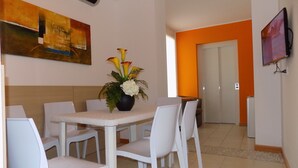 A dining area with a table and chairs, a vase with flowers, a painting on the wall, and a TV mounted on the wall. - Hotel Residence Sole (Fontanafredda)