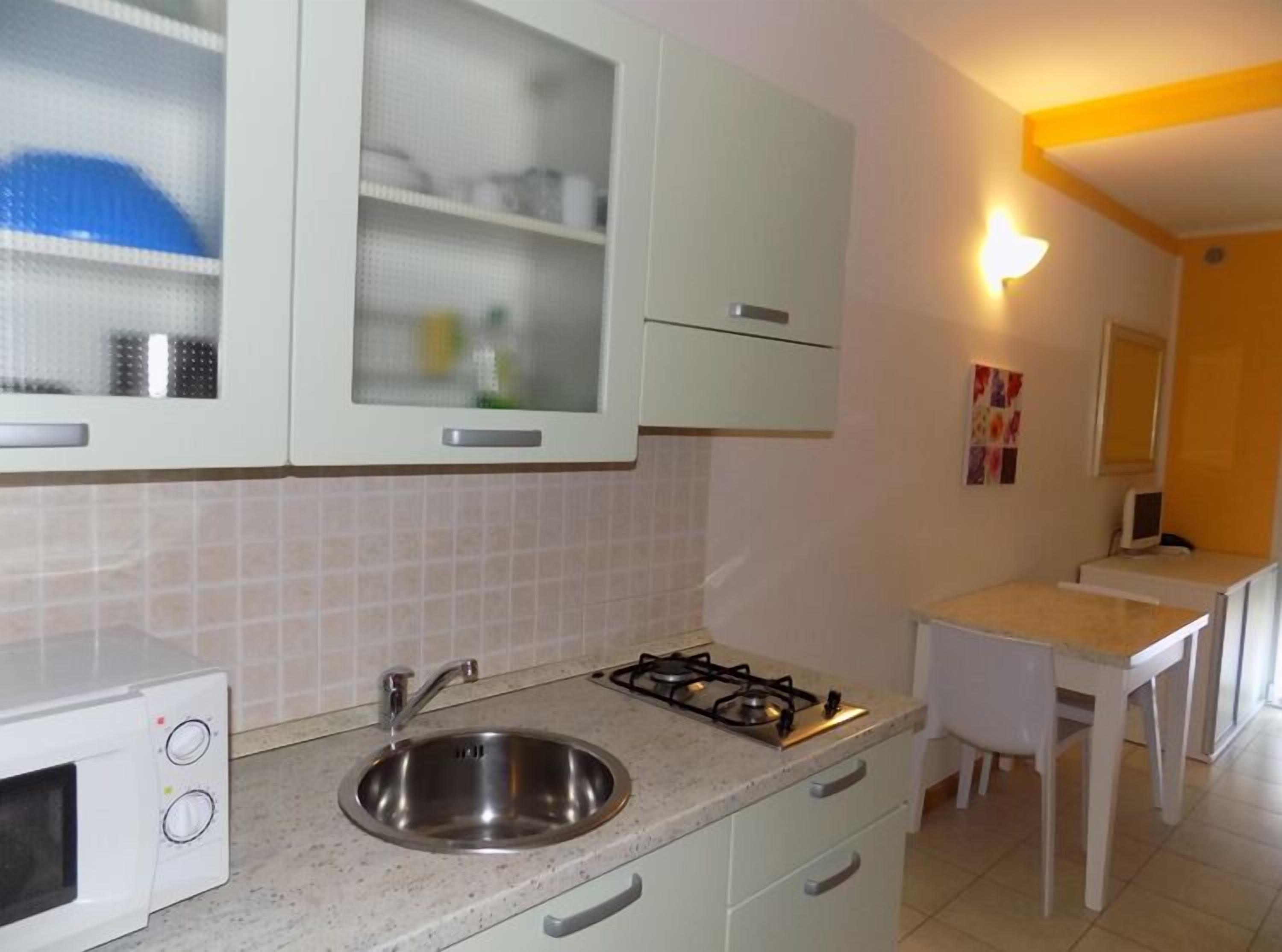 Cucina compatta con mobili bianchi, lavello in acciaio inossidabile, piano cottura a gas e un piccolo bancone.