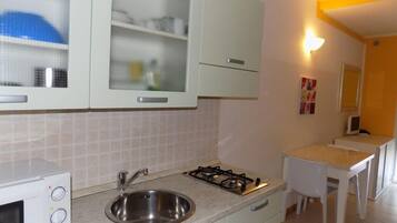 Cucina compatta con mobili bianchi, lavello in acciaio inossidabile, piano cottura a gas e un piccolo bancone.