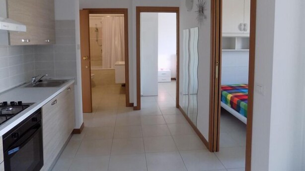A modern kitchen with a stove, oven, and sink, leading to a bathroom with a shower and toilet. - Hotel Residence Sole (Fontanafredda)