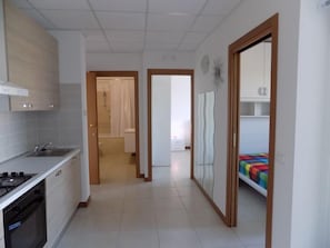A modern kitchen with a stove, oven, and sink, leading to a bathroom with a shower and toilet. - Hotel Residence Sole (Fontanafredda)