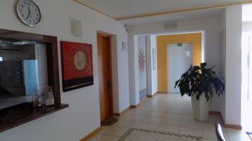 A hotel lobby with a clock, a reception desk, a large potted plant, and a patterned floor.