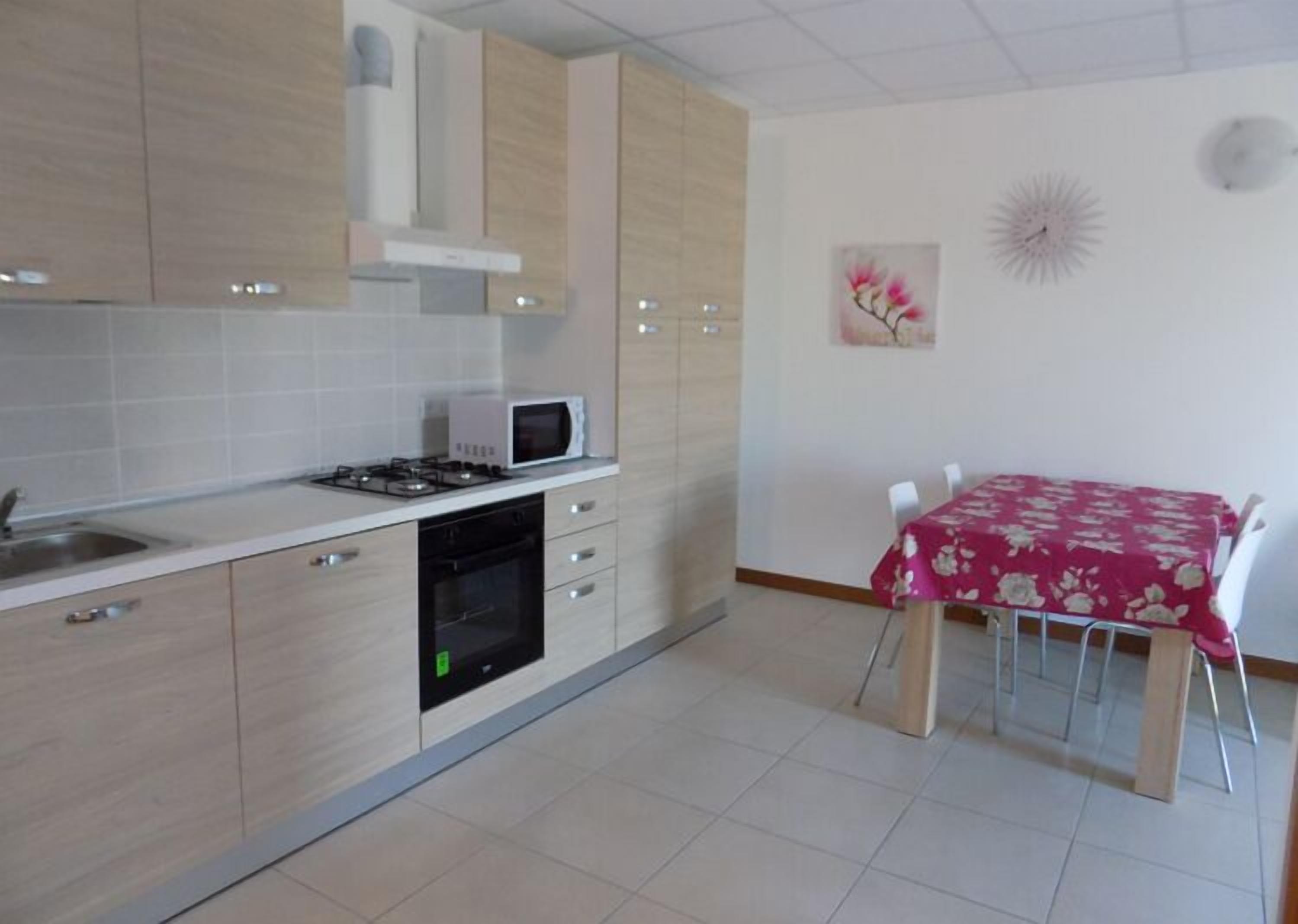 Une cuisine moderne équipée d’un four à micro-ondes, d’une cuisinière et d’un lave-vaisselle. On y trouve une table à manger avec des chaises et une nappe à motifs floraux.