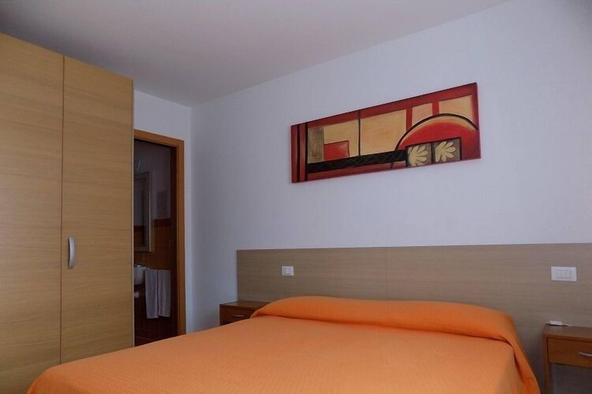 A hotel room with a bed, a wooden wardrobe, a nightstand, and a wall-mounted painting.