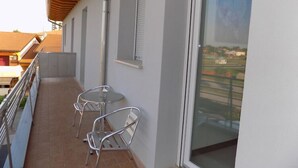 A balcony with two metal chairs, a glass table, and a view of a residential area through a large window. - Hotel Residence Sole (Fontanafredda)