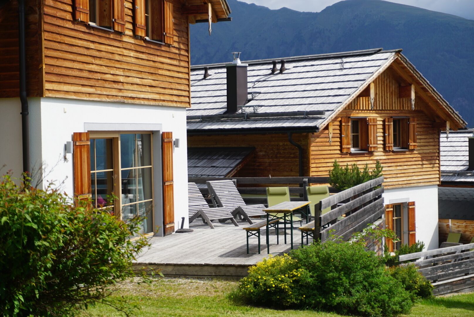 Un chalet en bois doté d’un balcon, d’un espace salon extérieur et offrant une vue sur les montagnes.