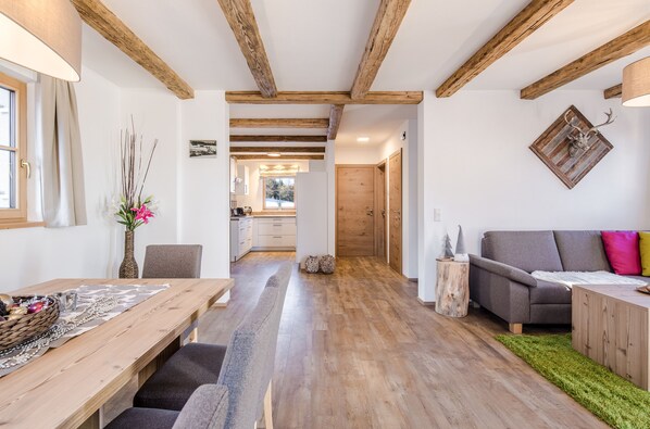 A spacious living area with a wooden dining table, a sofa, and a green rug. - Chaletdorf Fanningberg (Weisspriach)