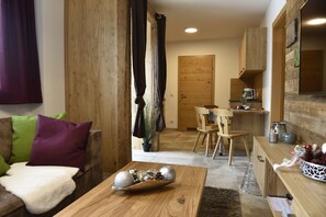 A cozy living room with a wooden coffee table, a sofa with colorful cushions, and a dining area with wooden chairs. - Chaletdorf Fanningberg (Weisspriach)