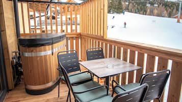 A wooden deck with a table and chairs, overlooking a snowy landscape with ski lifts.