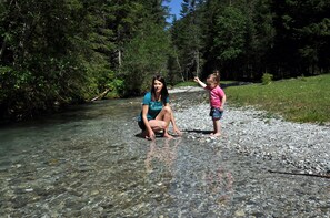 A woman and a child by a clear stream with pebbles, surrounded by dense forest. - Chaletdorf Fanningberg (Weisspriach)