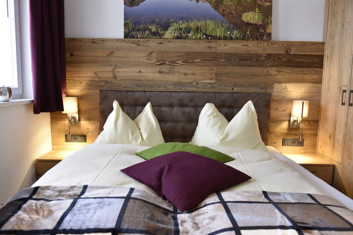 A bedroom with a wooden headboard, a bed with white and green pillows, and bedside lamps.