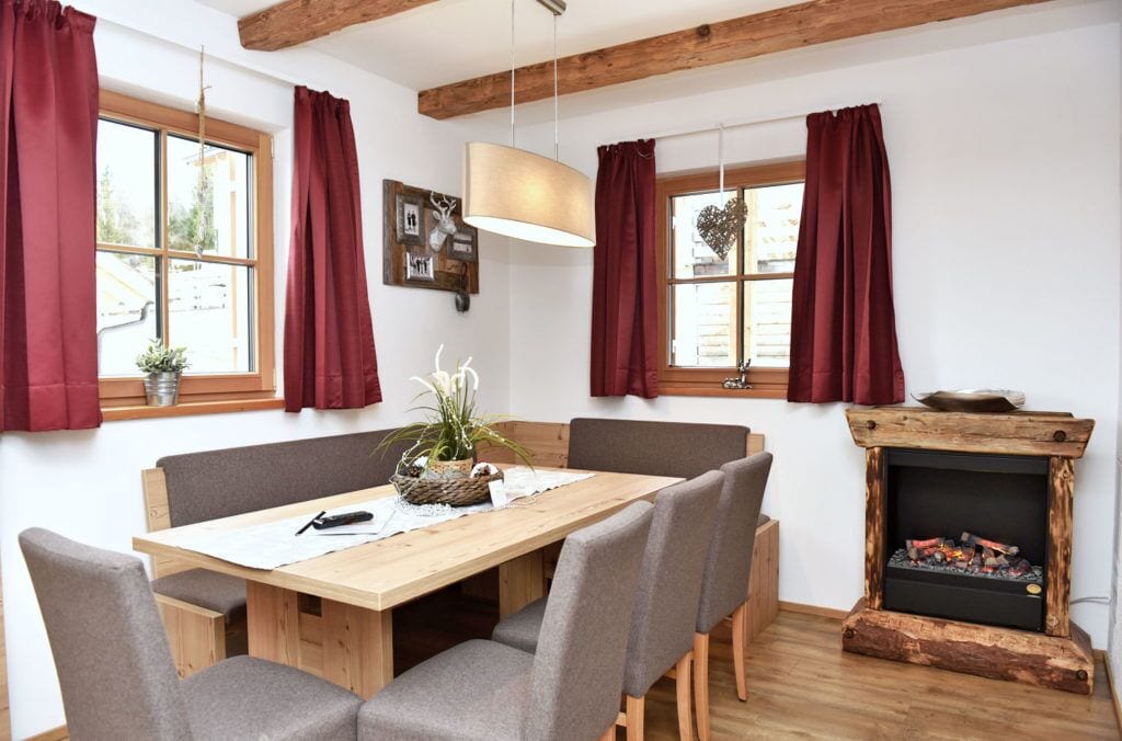 A dining area with a wooden table, grey upholstered chairs, and a fireplace with logs.