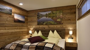 A wooden-paneled bedroom with a large bed, multiple pillows, bedside lamps, and framed landscape paintings on the walls. - Chaletdorf Fanningberg (Weisspriach)