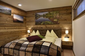 A wooden-paneled bedroom with a large bed, multiple pillows, bedside lamps, and framed landscape paintings on the walls. - Chaletdorf Fanningberg (Weisspriach)