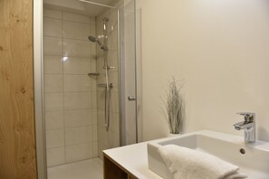 A modern bathroom with a glass-enclosed shower, a white sink with a chrome faucet, and a wooden vanity. - Chaletdorf Fanningberg (Weisspriach)