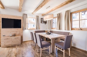 Un comedor con una mesa y sillas de madera, un televisor fijado en una pared de madera, y una ventana con cortinas.