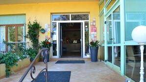 A hotel entrance with a tiled patio, potted plants, and a visible reception area. - Hôtel Cyrnea (Calvi)