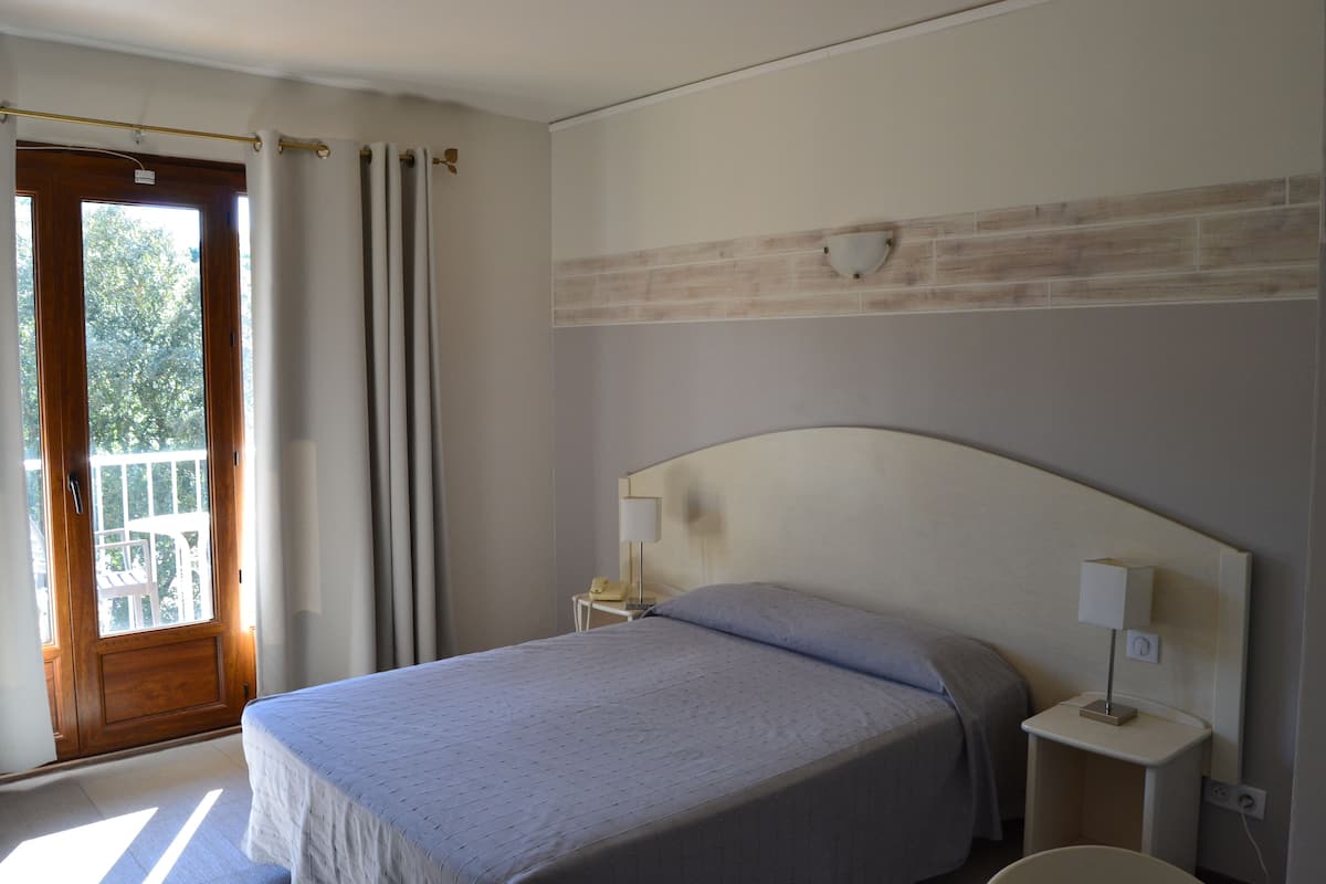 A hotel room with a bed, a nightstand, a lamp, and a window with curtains.
