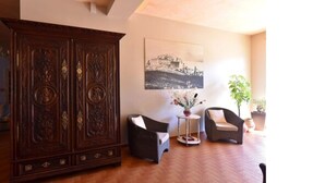 A living room with a large wooden cabinet, two wicker chairs, a small table with a vase of flowers, and a framed picture on the wall. - Hôtel Cyrnea (Calvi)