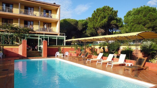 A pool area with lounge chairs, a building with balconies, and a covered seating area. - Hôtel Cyrnea (Calvi)