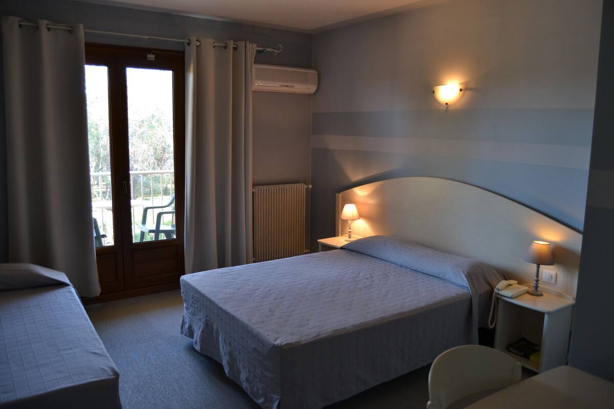 A hotel room with two beds, a window with curtains, an air conditioning unit, a bedside lamp, a phone, and a chair.