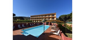 A hotel with a swimming pool, outdoor seating, and a building with multiple balconies. - Hôtel Cyrnea (Calvi)