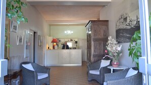 A hotel lobby with wicker furniture, a reception desk, and a chandelier. - Hôtel Cyrnea (Calvi)