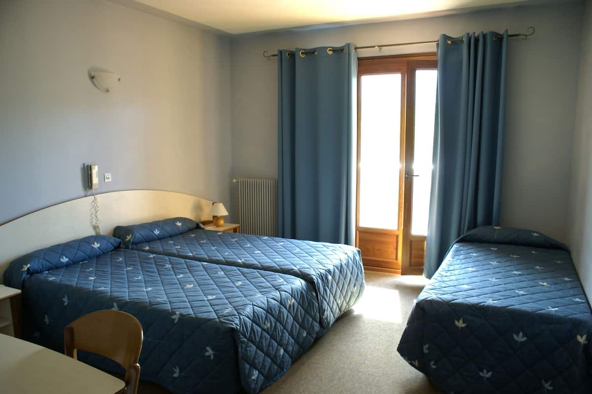 A bedroom with two beds, a chair, a table, a lamp, and a window with curtains.