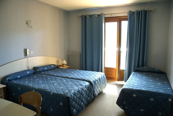 Une chambre avec deux lits, une chaise, une table, une lampe et une fenêtre avec des rideaux.
