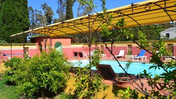 A pool area with a yellow canopy, lounge chairs, and a small garden area.