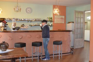 A bar area with stools, a counter, and shelves with bottles. - Hôtel Cyrnea (Calvi)