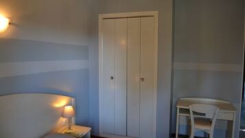 Een slaapkamer met een bed, een nachtkastje met lamp, een kledingkast en een bureau met stoel.